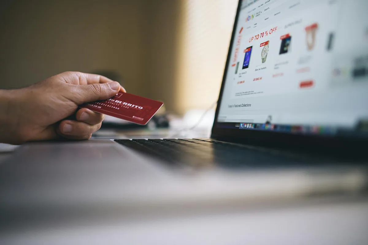 Person browsing an online store and holding a credit card next to open laptop.